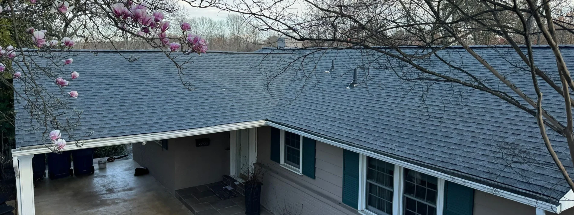 An aerial photo of an L-shaped single-story home with a dark gray shingled roof and white gutters.