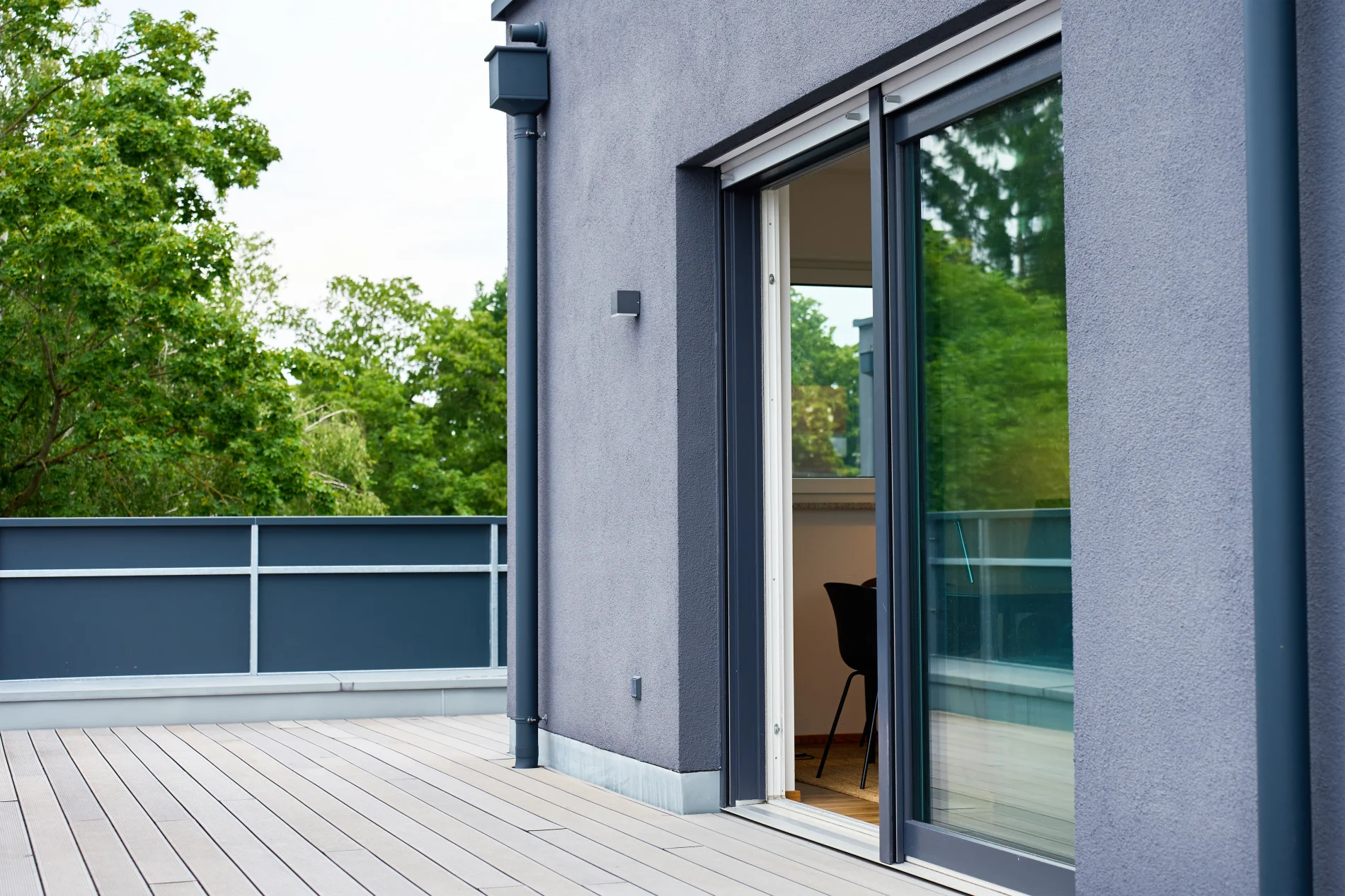 A sliding patio door with a white frame and blue trim. The home it is installed in has a blue exterior, and the deck it opens onto has a light-colored wooden surface.